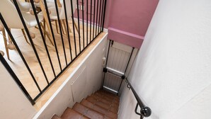 Uma escadaria com degraus de madeira e corrimãos de metal preto, que leva a um quarto com paredes brancas e uma parede em tons de rosa.