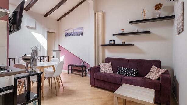 Uma sala de estar moderna com um sofá roxo, piso de madeira e uma pintura com vista para a cidade na parede.