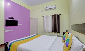 A hotel room with a bed, a flat-screen TV mounted on the wall, an air conditioning unit, and a door. - Guru Comfort, 100 m from Apollo Hospital (Bengaluru)
