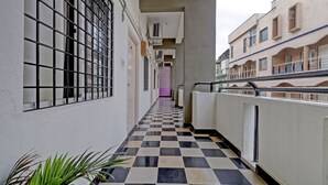 A narrow corridor with a checkered floor, barred windows, and a view of adjacent buildings. - Guru Comfort, 100 m from Apollo Hospital (Bengaluru)