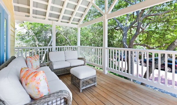 A covered porch with a white railing, wicker furniture, and a view of trees and parked cars. - 100 Yards to Beach with Gulf View, Large Sundeck, and Bikes (Santa Rosa Beach)