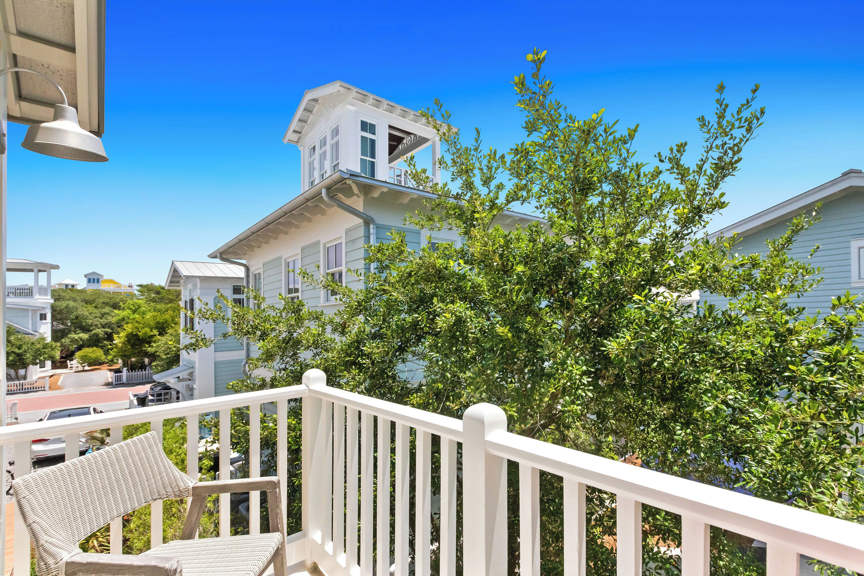 A balcony with a white railing, a wicker chair, and a tree in the background.