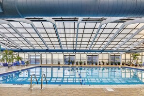 Une piscine intérieure dotée d’un toit en verre, de chaises bleues placées au bord du bassin et de plantes en pot.