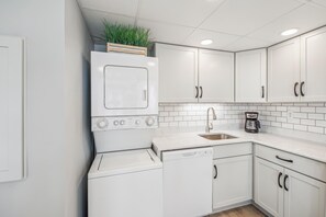 Une cuisine moderne avec des meubles blancs, un lave-vaisselle encastré, une machine à café et une plante posée sur le réfrigérateur.