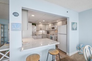 Une cuisine moderne avec des meubles blancs, un plan de travail en marbre et un four à micro-ondes encastré.