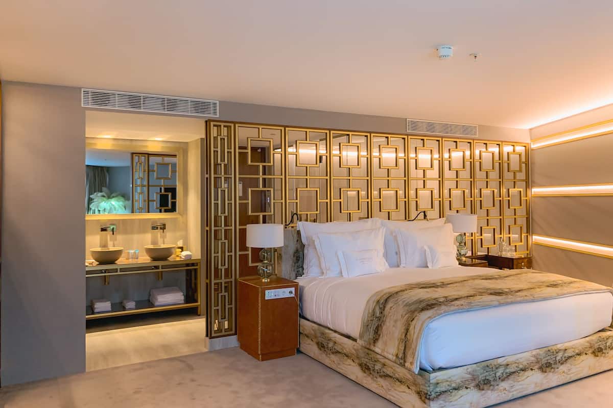 Une chambre d’hôtel moderne avec un grand lit, une coiffeuse avec un miroir et un panneau décoratif au mur.