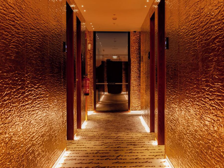 A hallway with textured walls and a patterned carpet leading to a dark room.