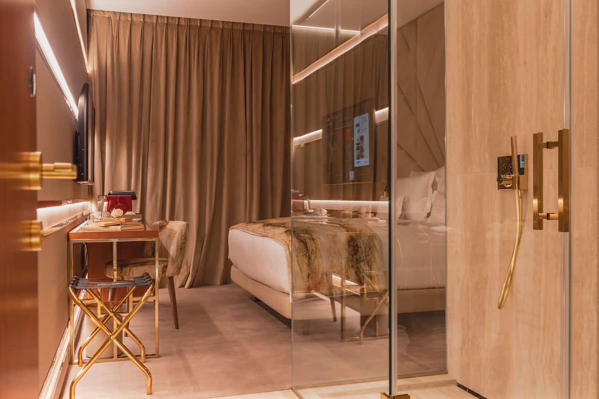 Une chambre d’hôtel moderne avec une cloison en verre, un lit, un bureau avec une chaise et une armoire.
