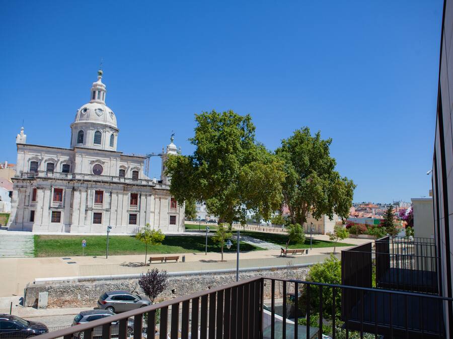 A historic building with a prominent dome and classical architecture, situated in a green urban area with trees and a clear sky.