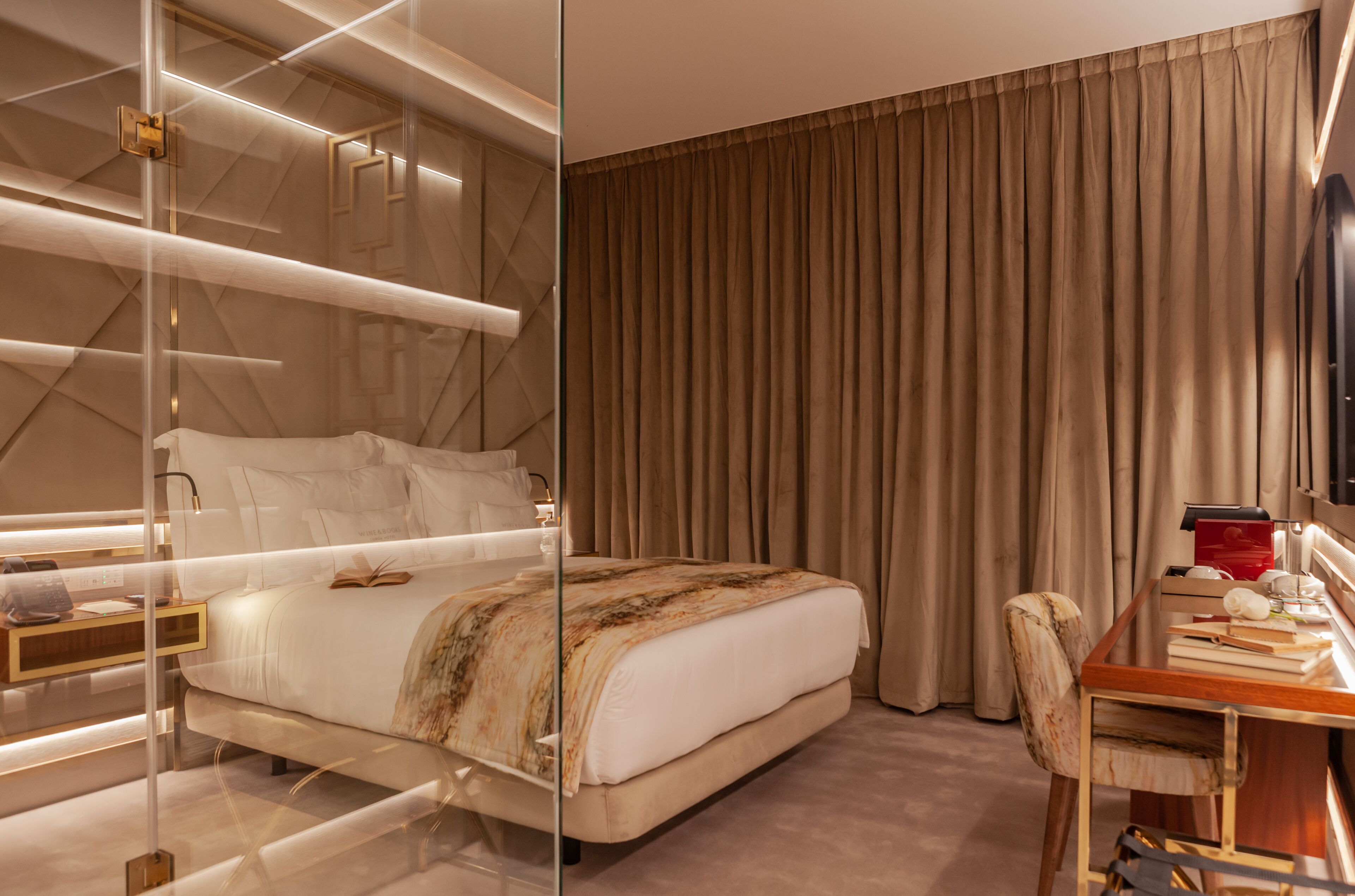 A modern hotel room with a large bed, a desk with a chair, and a large window with curtains.
