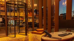 Un hall d’hôtel doté d’une porte tournante, d’un comptoir de réception avec un ordinateur, et offrant une vue sur la rue.