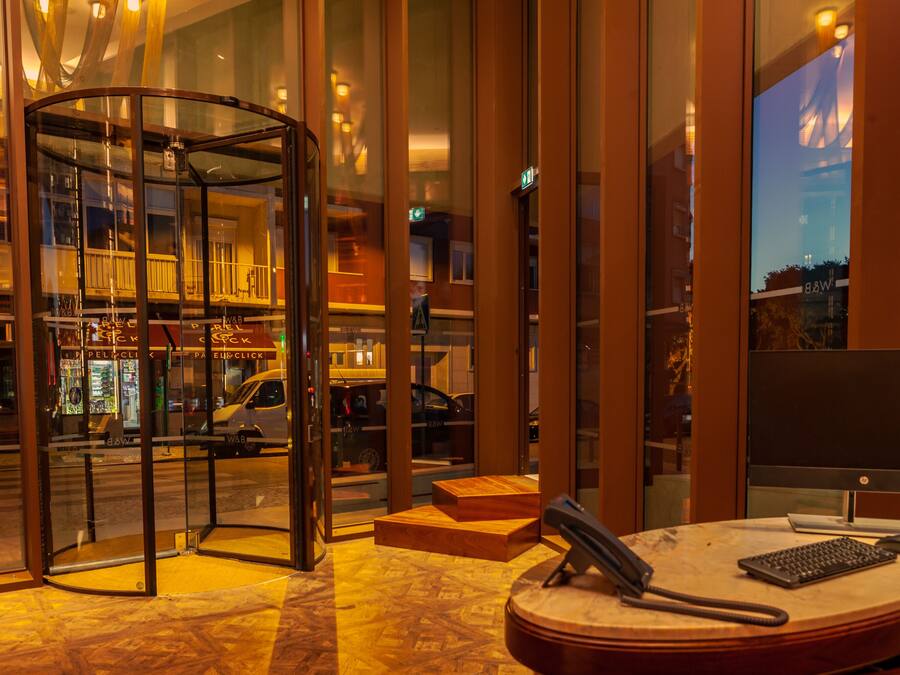 Een hotel lobby met een draaideur, een receptiebalie met een computer, en uitzicht op de straat.
