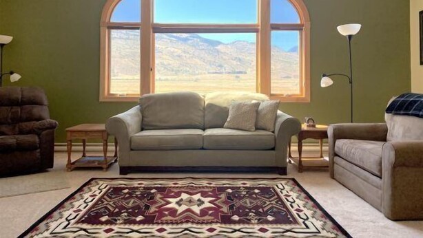 A living room with a large arched window, a patterned rug, and two side tables. - Windsor Drive Monthly Rental (Cody)