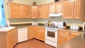 A kitchen with wooden cabinets, a white dishwasher, a stove, and a toaster. - Windsor Drive Monthly Rental (Cody)