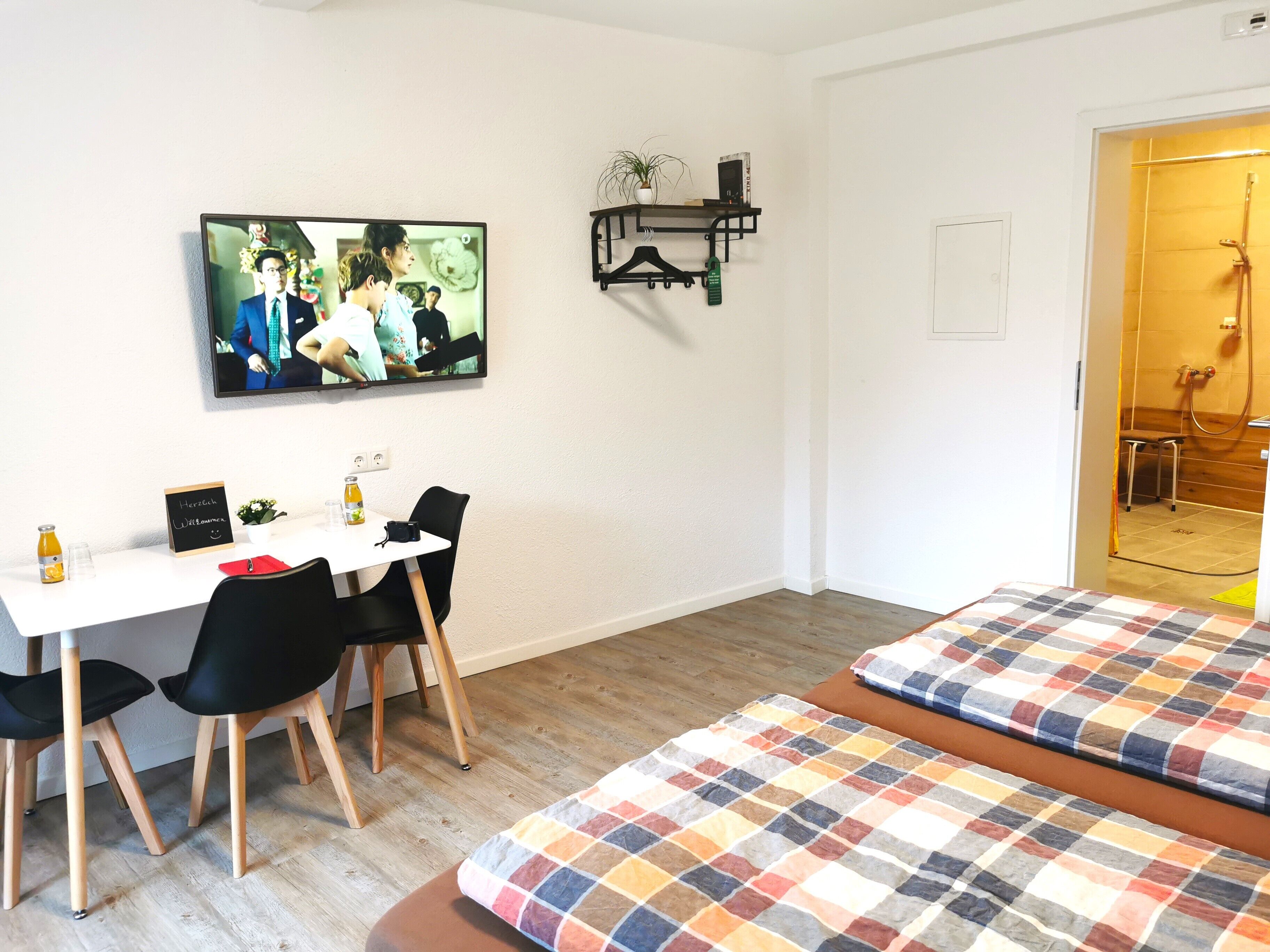 A hotel room with a bed, a desk with chairs, a television, and a shower area.