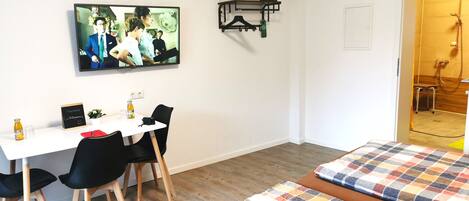 A hotel room with a bed, a desk with chairs, a television, and a shower area.