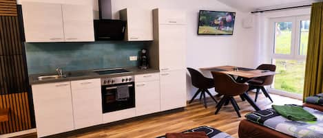 Una cocina compacta con comedor, horno empotrado y televisor montado en la pared.