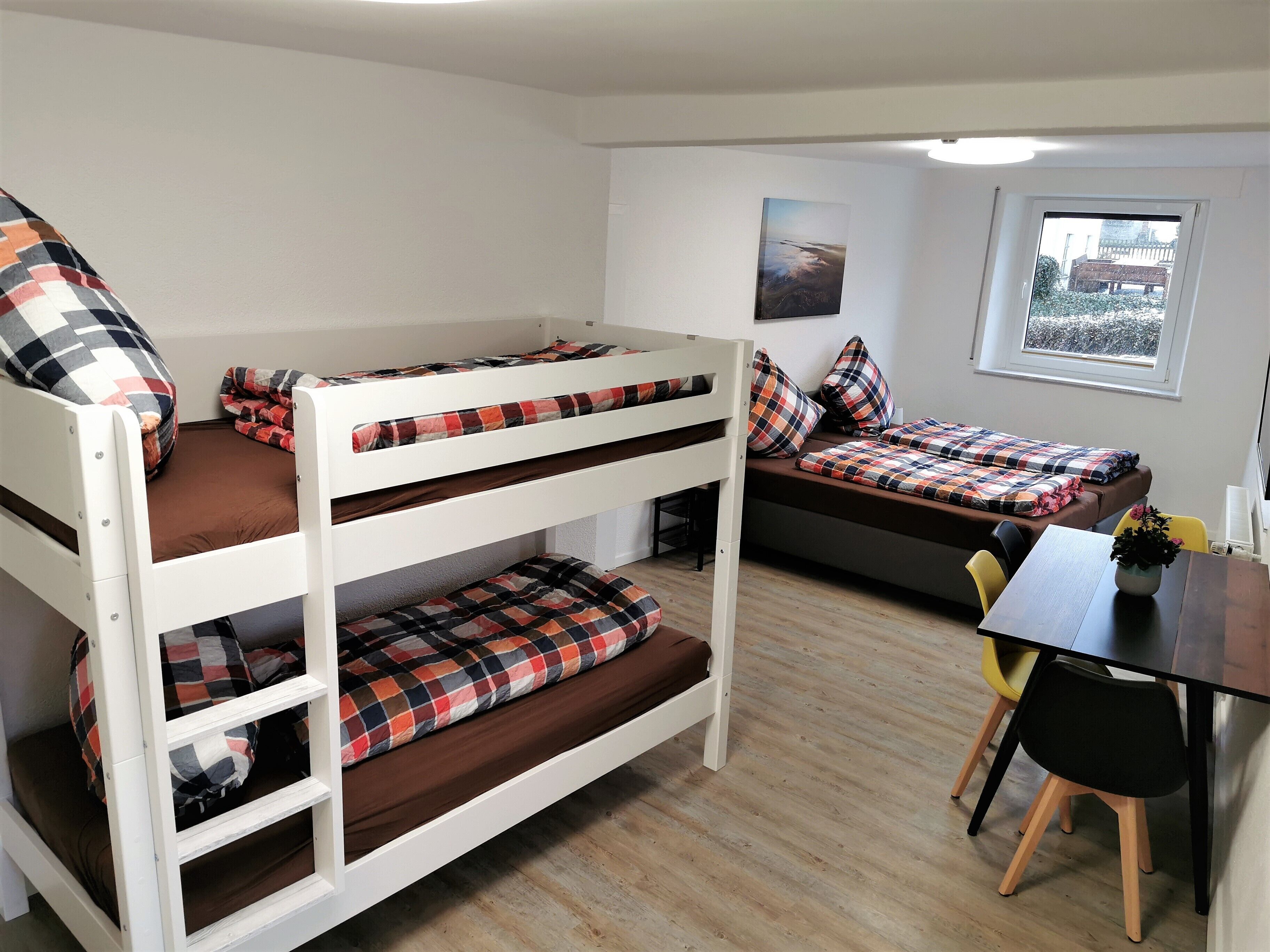 A dormitory room with bunk beds, a desk, and a window.