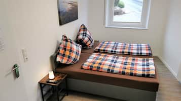 A small, cozy room with a bed, a window, a lamp, and a small table with a remote control.