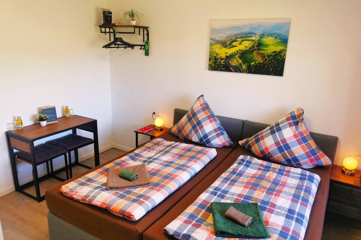A room with two beds, a desk, a chair, a small table, and a painting on the wall.