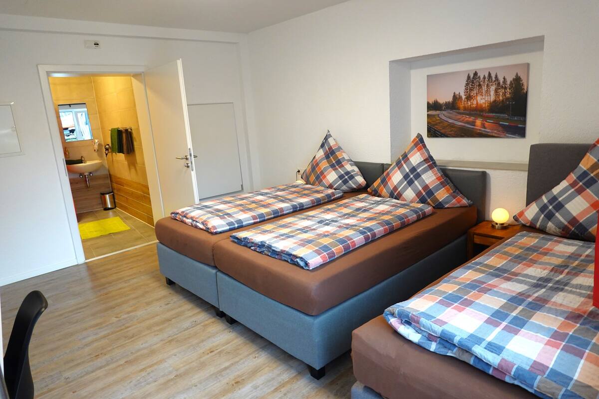 A bedroom with two beds, a bathroom, and a hallway.
