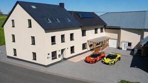 A modern two-story building with a garage, two sports cars, and a solar panel on the roof. - Speedy's Bed & Breakfast (Reimerath)