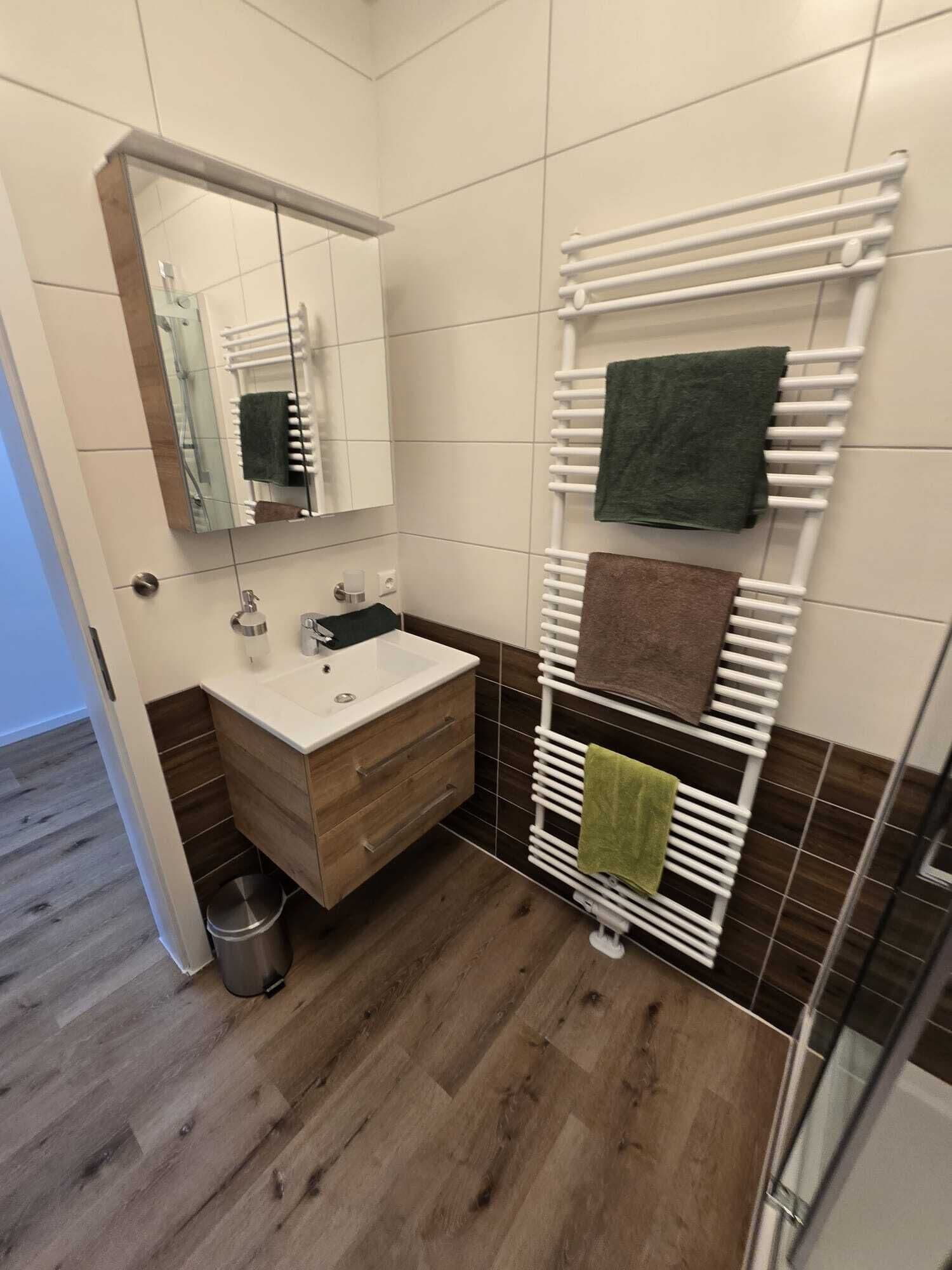 A bathroom with a wooden vanity, a mirror, a white towel rack, and a shower area.