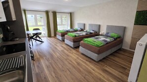 A modern room with three beds, a kitchenette, and a dining area. - Speedy's Bed & Breakfast (Reimerath)