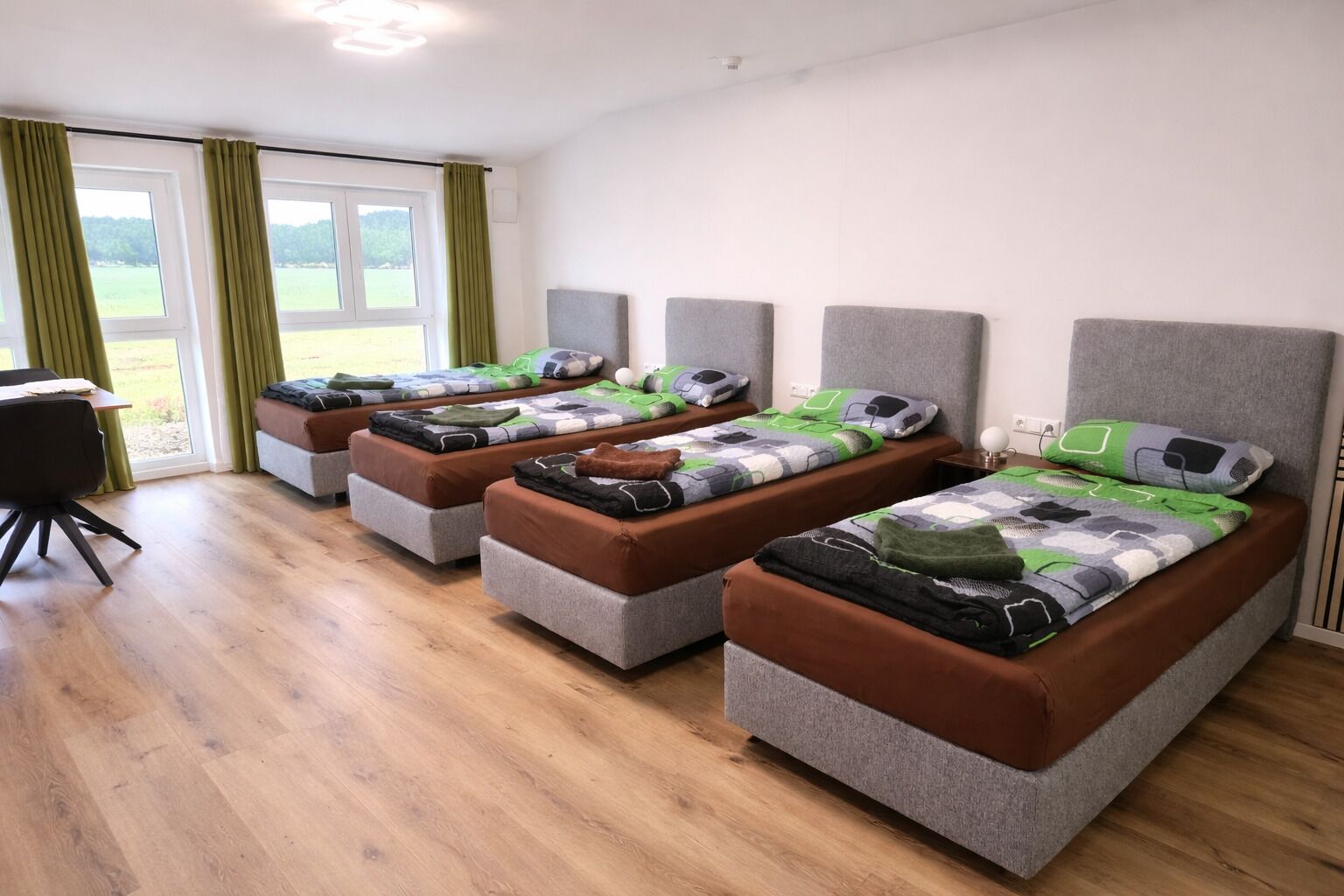 Una habitación con cuatro camas individuales, un escritorio y una silla.