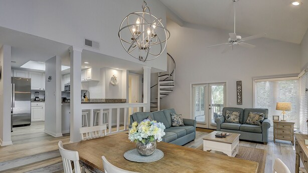 A spacious living area with a dining table, a sofa, a chandelier, and a ceiling fan. - Sunset Rentals | St. Andrews 1662 (Hilton Head Island)