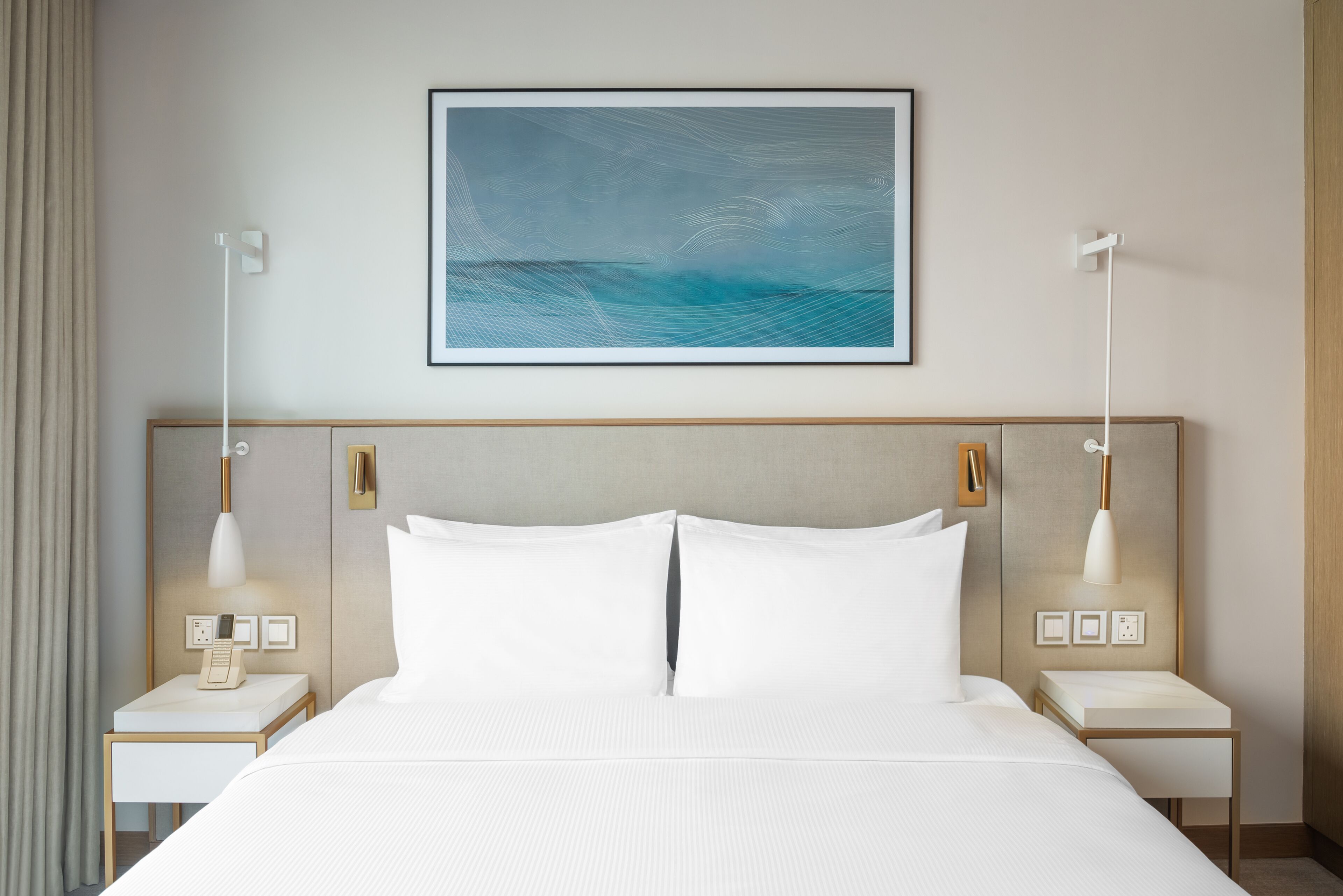 Habitación de hotel con una cama grande, dos mesitas de noche, una obra de arte en la pared y una lámpara moderna.