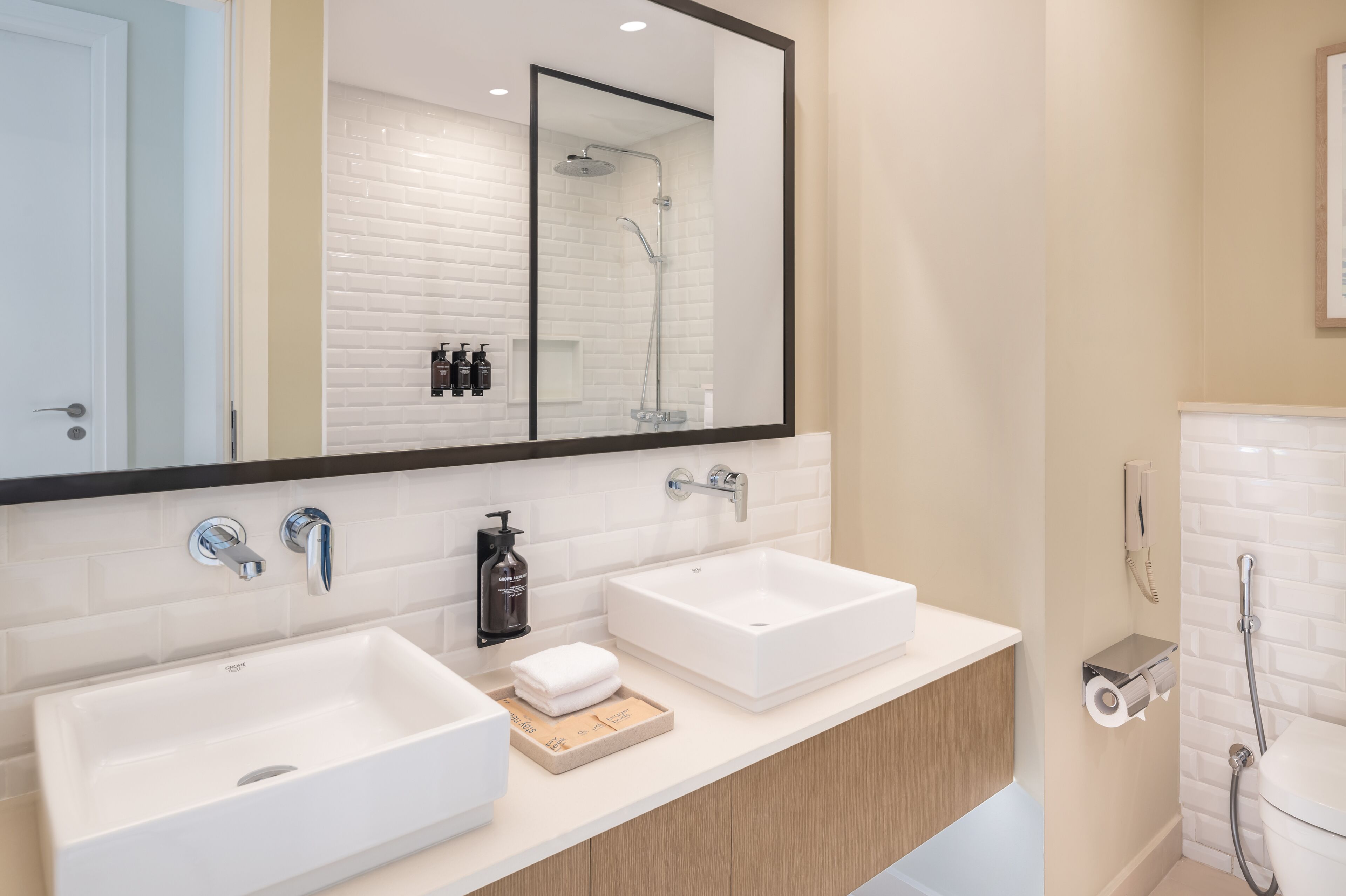 A modern bathroom with two sinks, a large mirror, and a shower.
