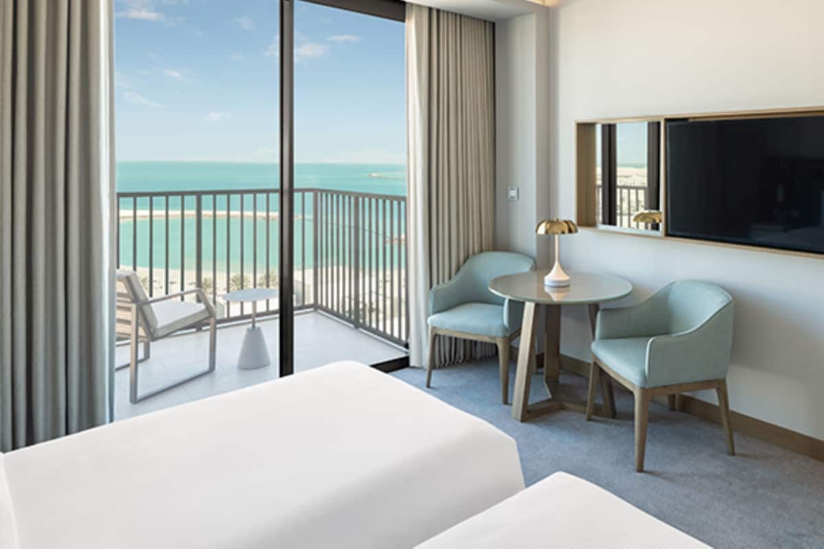 Quarto de hotel com varanda, duas cadeiras, uma mesa pequena e uma cama.