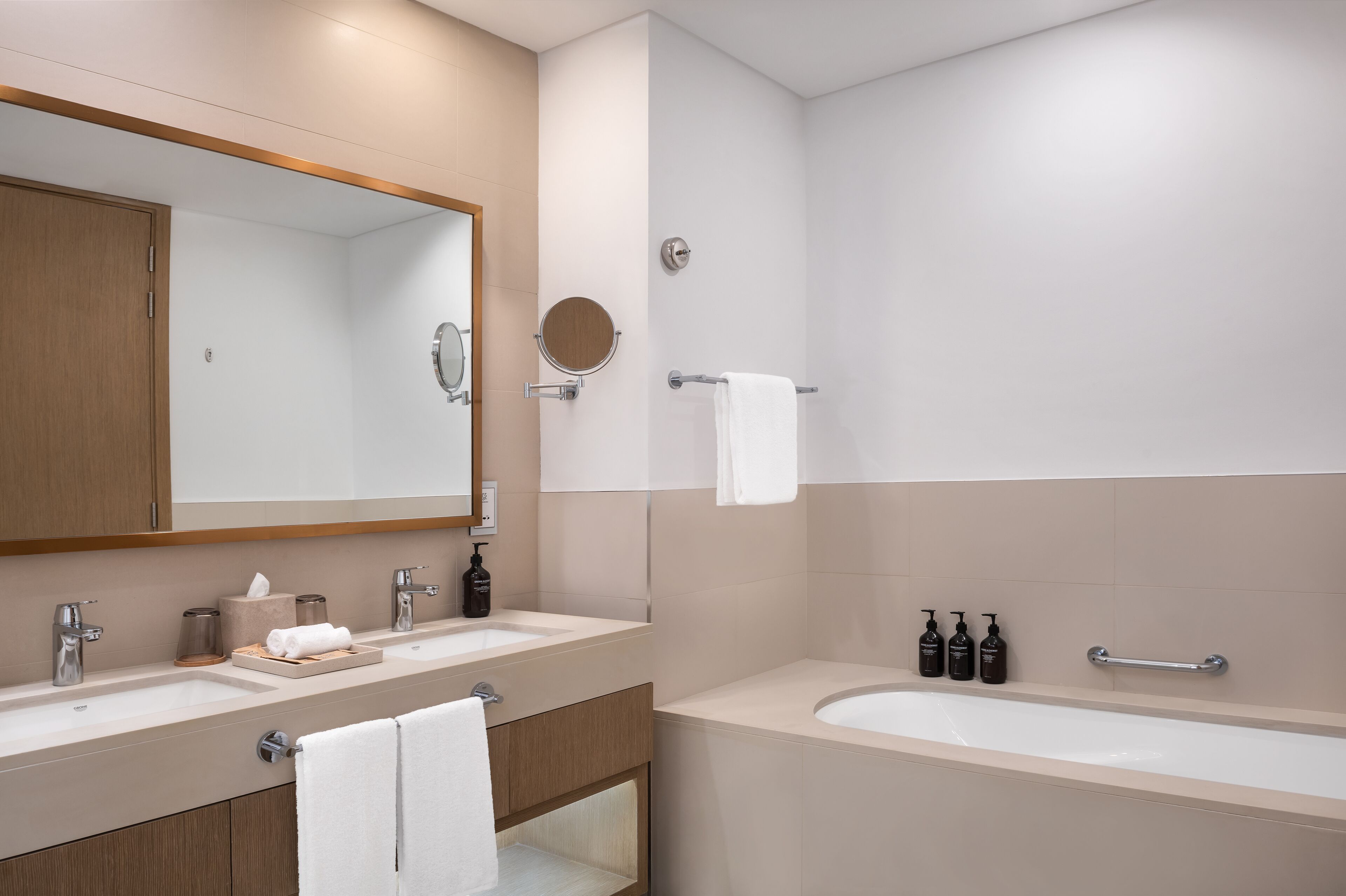 Un baño moderno con dos lavamanos, un espejo grande, un espejo redondo, una ducha y una bañera.