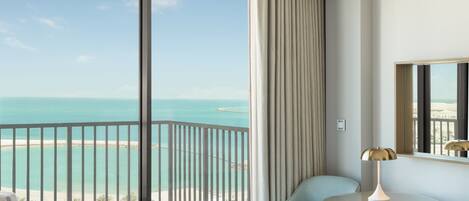 A hotel room with a large balcony, a bed, two chairs, a small table, and a lamp.