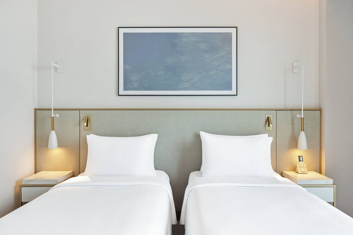 Quarto de hotel com duas camas, uma obra de arte emoldurada acima e abajures nas mesas de cabeceira.