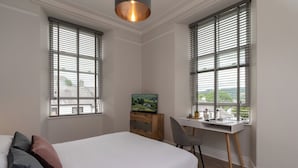 Une chambre à coucher avec un lit, un bureau et deux fenêtres équipées de stores.