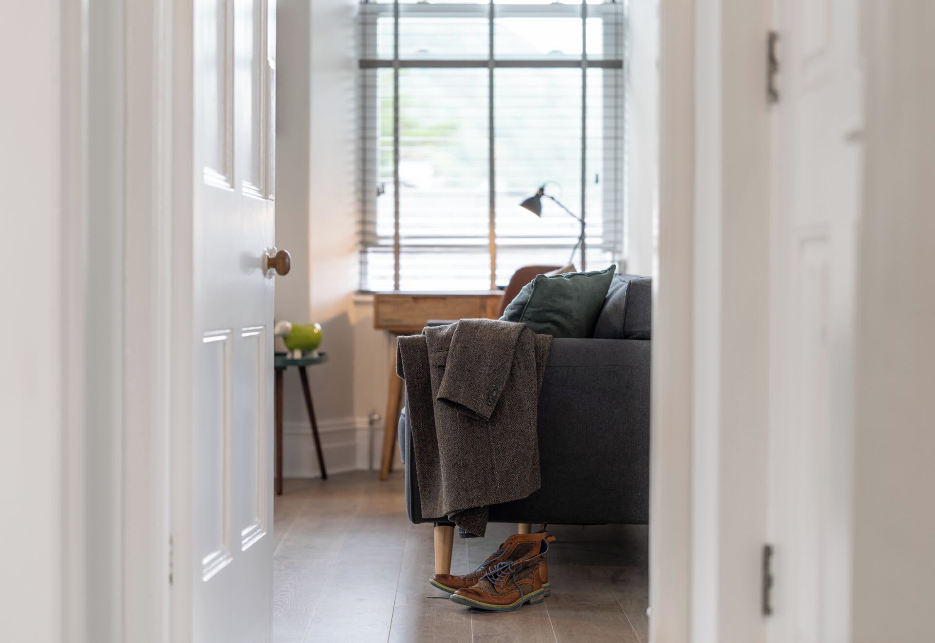 A hallway leading to a living room with a sofa, a lamp, and a pair of shoes on the floor.