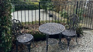 Une terrasse avec une table et deux chaises, entourée d’une clôture en métal et recouverte de gravier.
