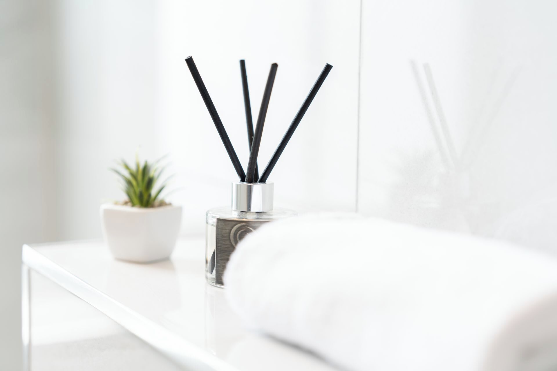Un comodino bianco con una piccola pianta in vaso e una bottiglia di diffusore di fragranze.