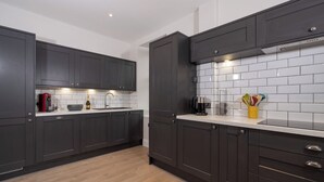 Une cuisine moderne avec des meubles de couleur sombre, un dosseret en carreaux blancs rectangulaires et un plancher en bois.