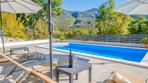 Ein Poolbereich mit Liegestühlen, einem Tisch mit Flasche und Glas sowie Blick auf Berge.