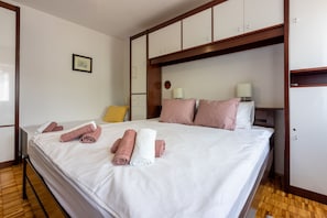 Een net opgemaakt bed met opgerolde handdoeken, een nachtkastje met lamp en een kledingkast in een hotelkamer.