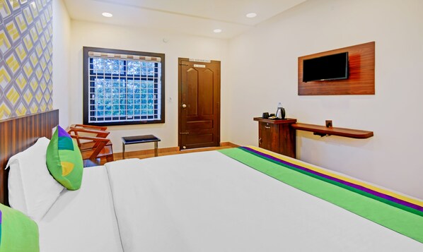 Habitación de hotel con cama, escritorio, televisor montado en la pared y ventana con vista a árboles.