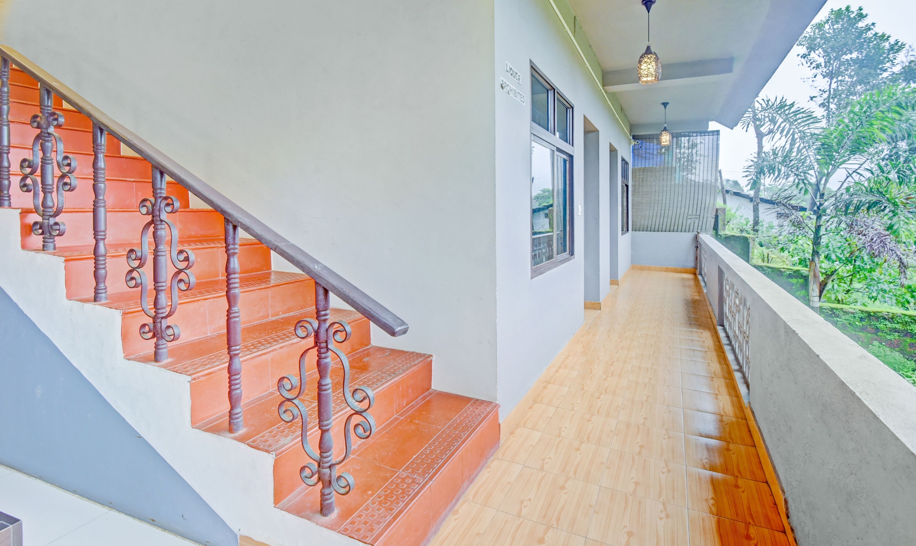 A staircase with ornate metal railings and orange steps, leading to a balcony with a wooden floor and a view of greenery.