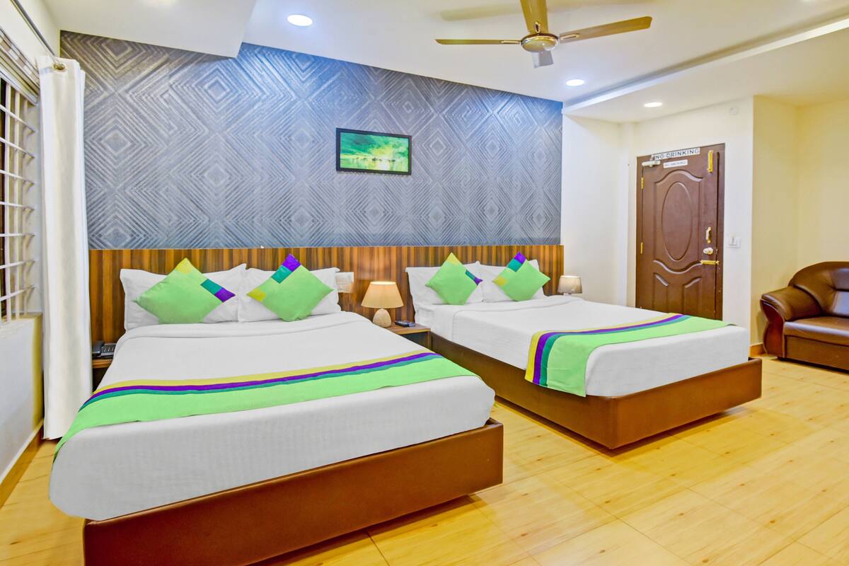 A hotel room with two beds, a wooden floor, a ceiling fan, a TV, and a door with a 'No Drinking' sign.