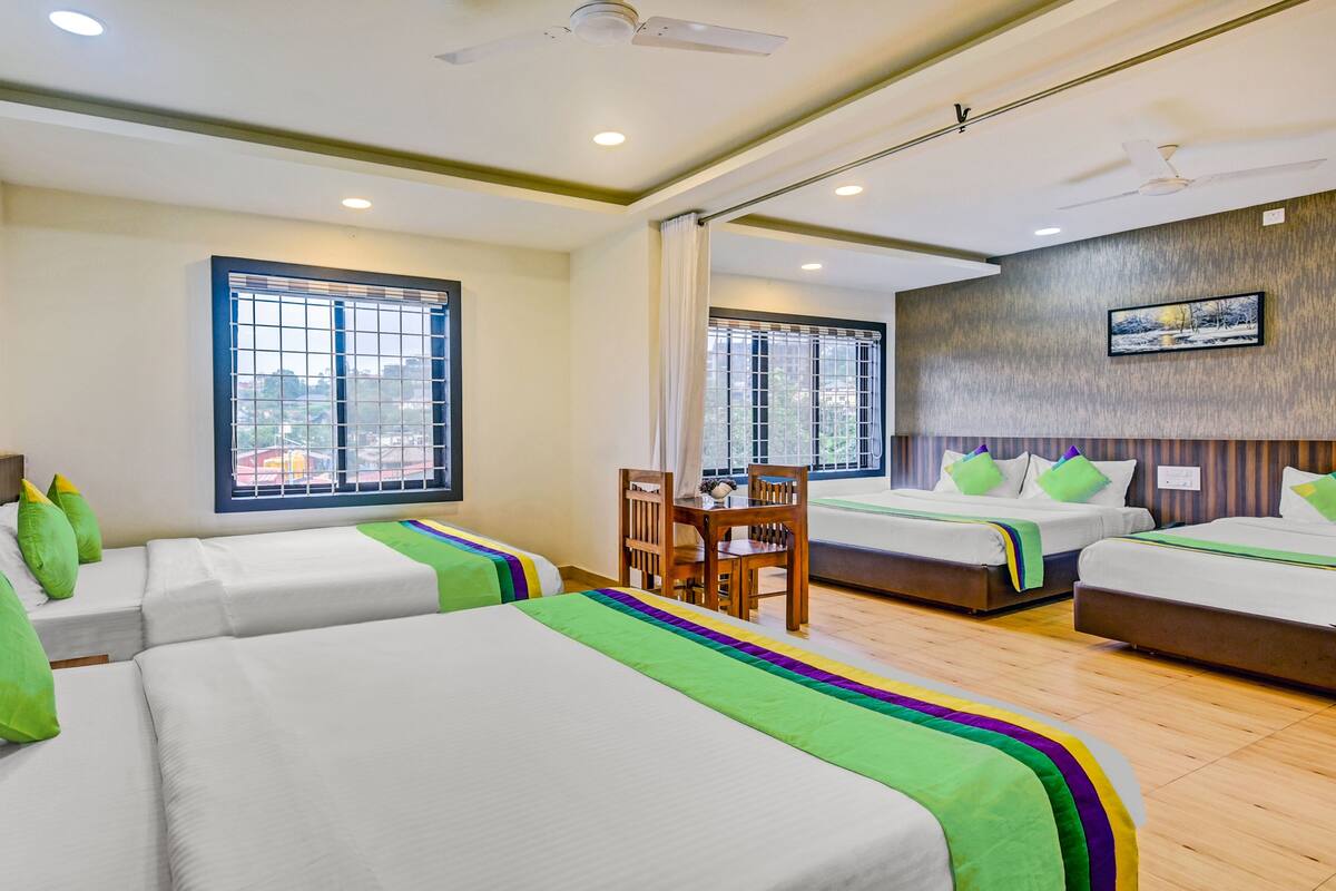 A hotel room with two single beds, a dining table, and a view of the city.