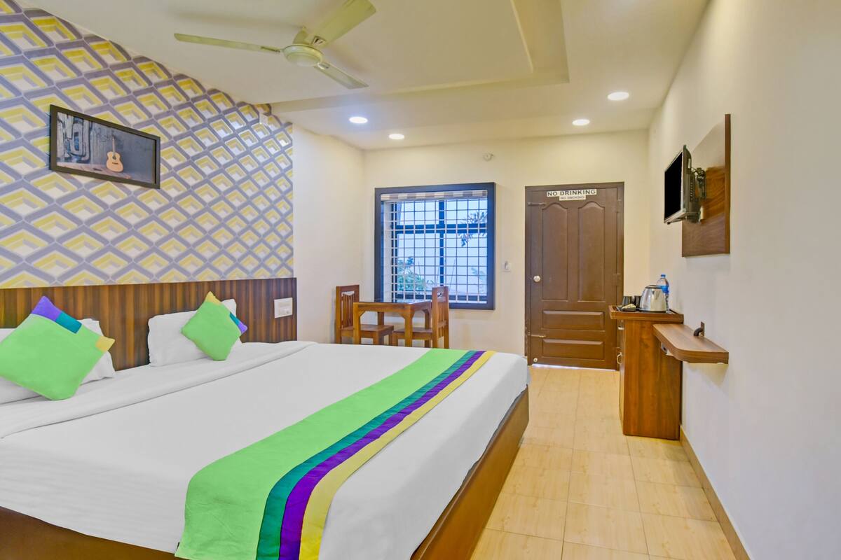 A hotel room with a bed, a desk, a chair, a window, and a door.