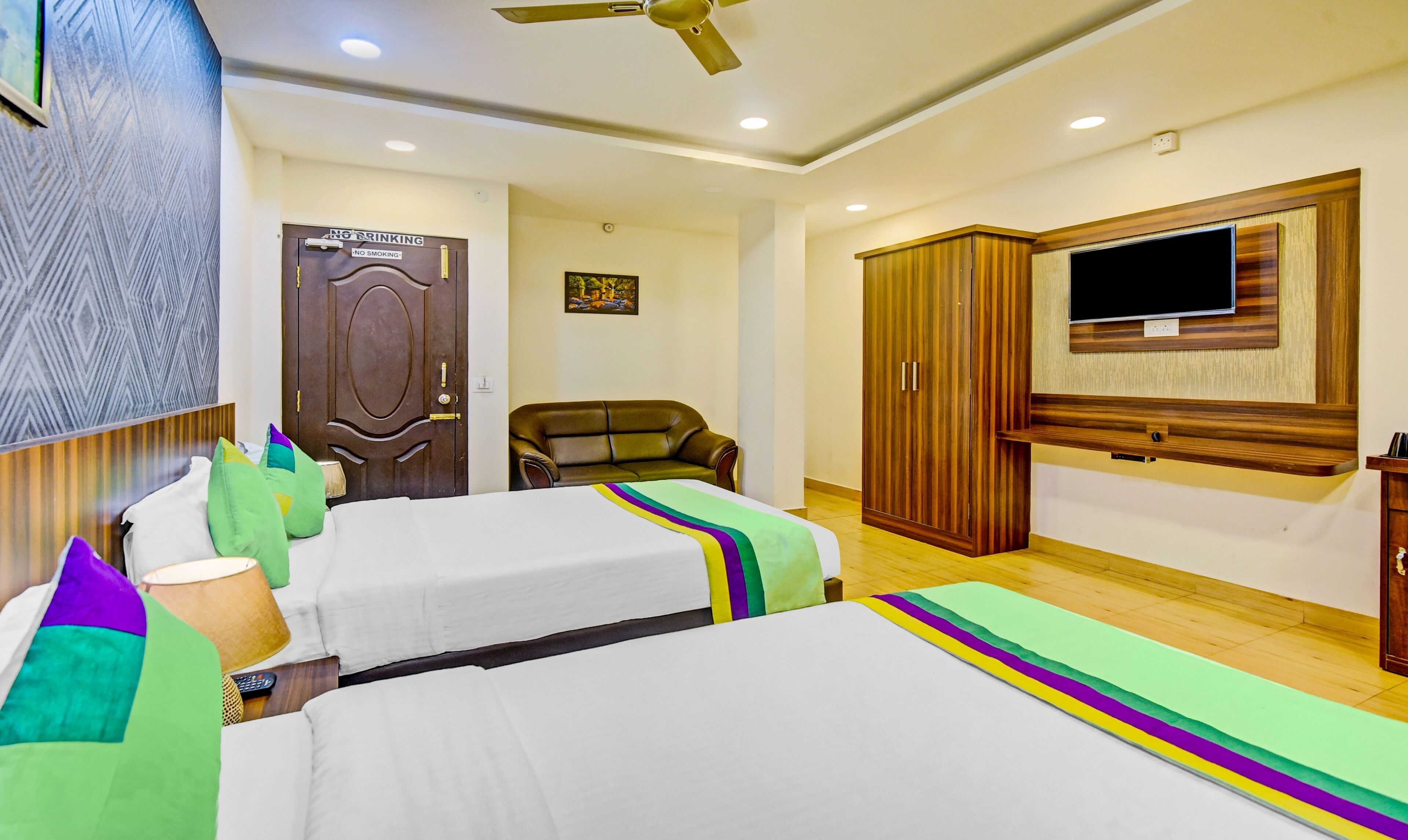 Quarto de hotel com duas camas, televisão, guarda-roupa e porta com sinais de proibição de fumar e beber.