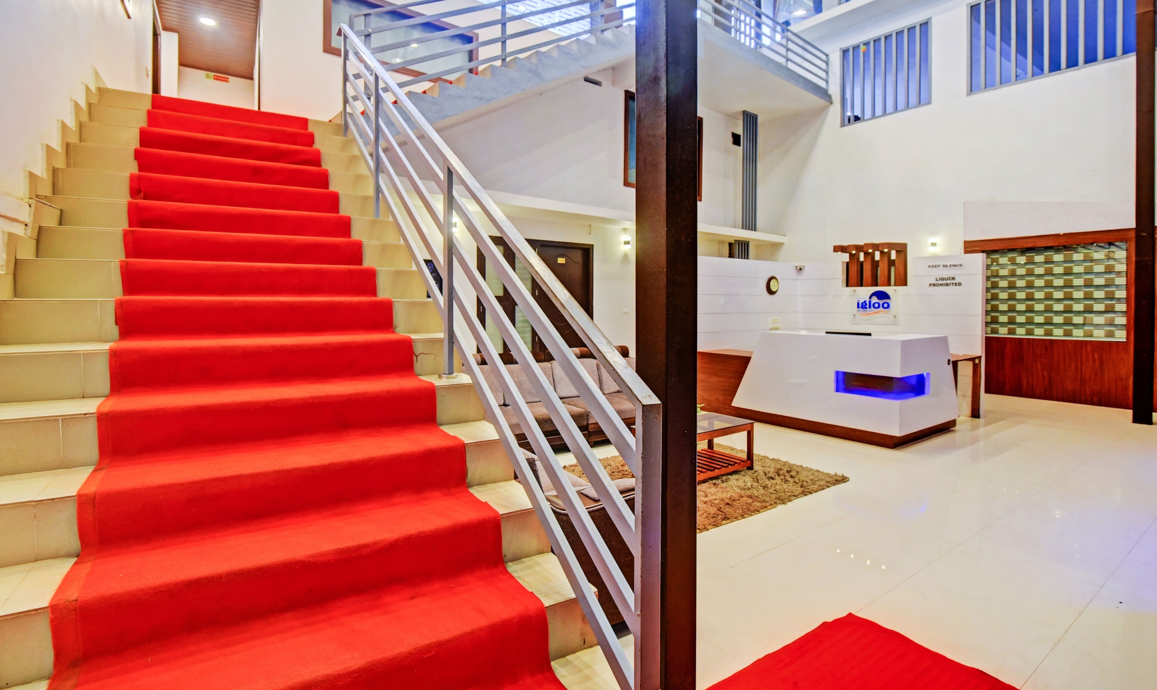 Una escalera con alfombra roja que conduce a un área de recepción de diseño moderno, con un mostrador y un letrero que dice 'Keep Silence'.